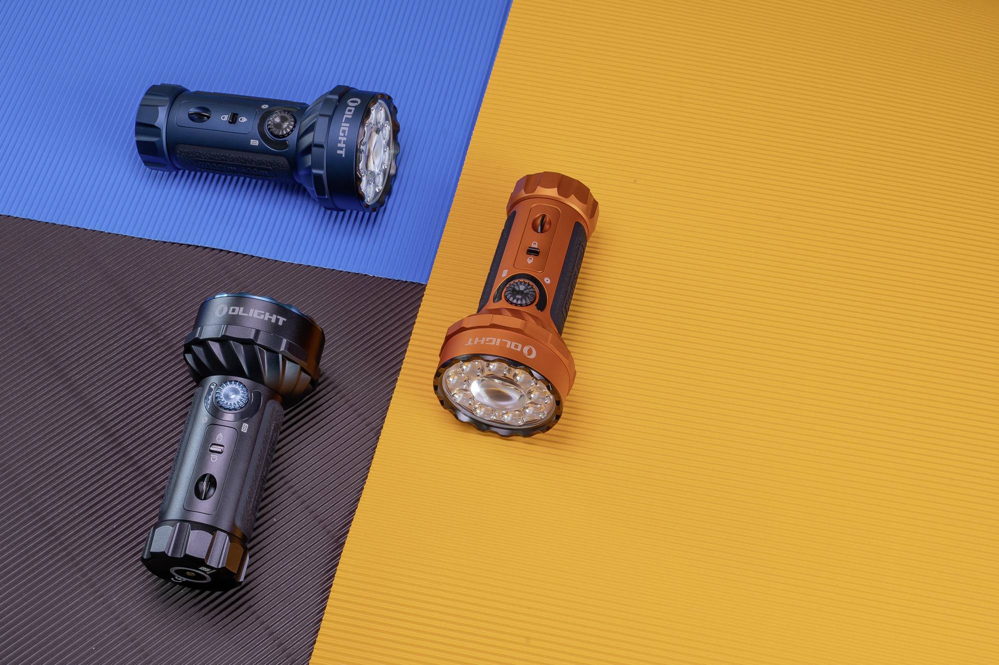 Drei tragbare Taschenlampen, eine blaue, eine schwarze und eine orangefarbene, liegen auf farbigem Hintergrund in Blau, Braun und Orange.