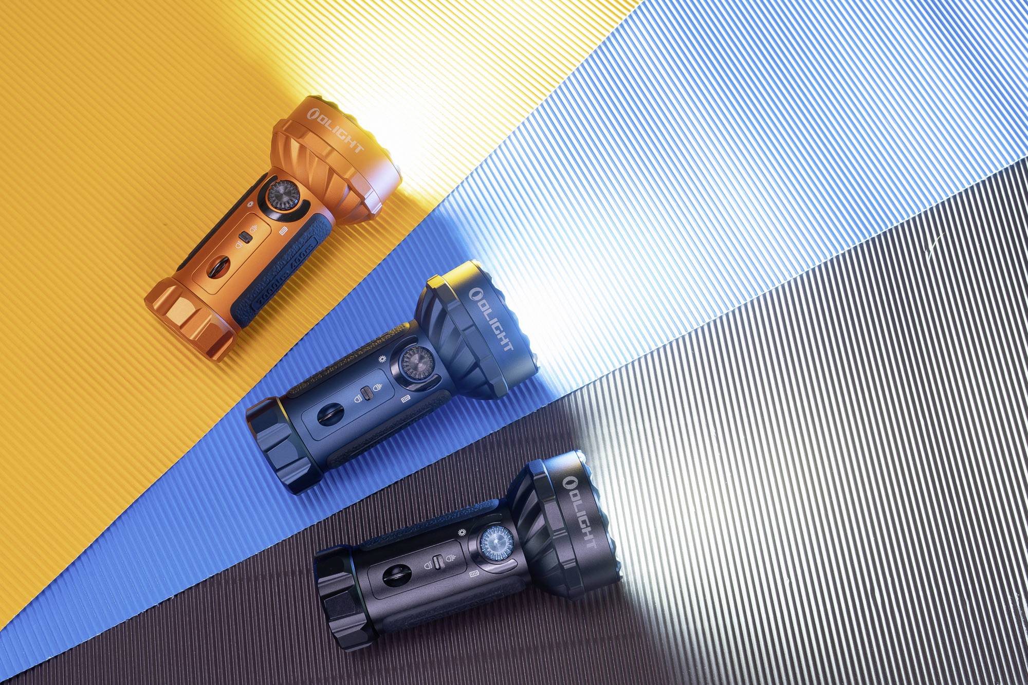 Drei Taschenlampen strahlen Licht unterschiedlicher Farben auf gestreiftem Hintergrund. Oben orange, Mitte dunkelblau, unten schwarz.