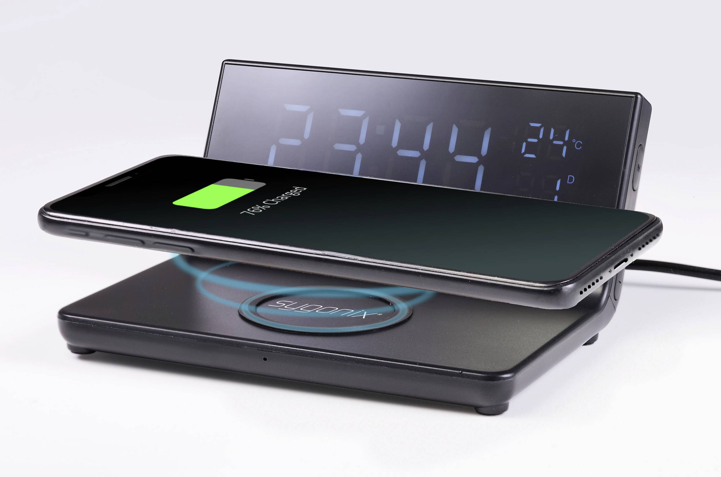 Ein Smartphone lädt drahtlos auf einem Ladegerät. Im Hintergrund zeigt eine Digitaluhr die Zeit '23:44' und die Temperatur '24°C' an.
