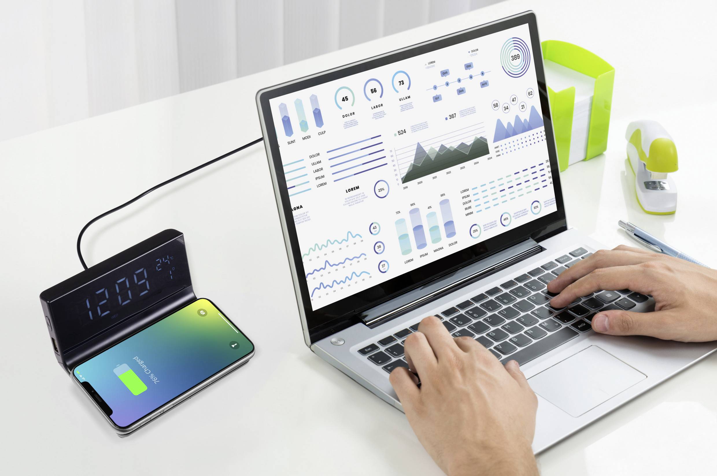 Eine Person tippt auf einem Laptop mit Datendiagrammen auf dem Bildschirm. Rechts daneben lädt ein Smartphone kabellos mit 12:09 Uhr auf.