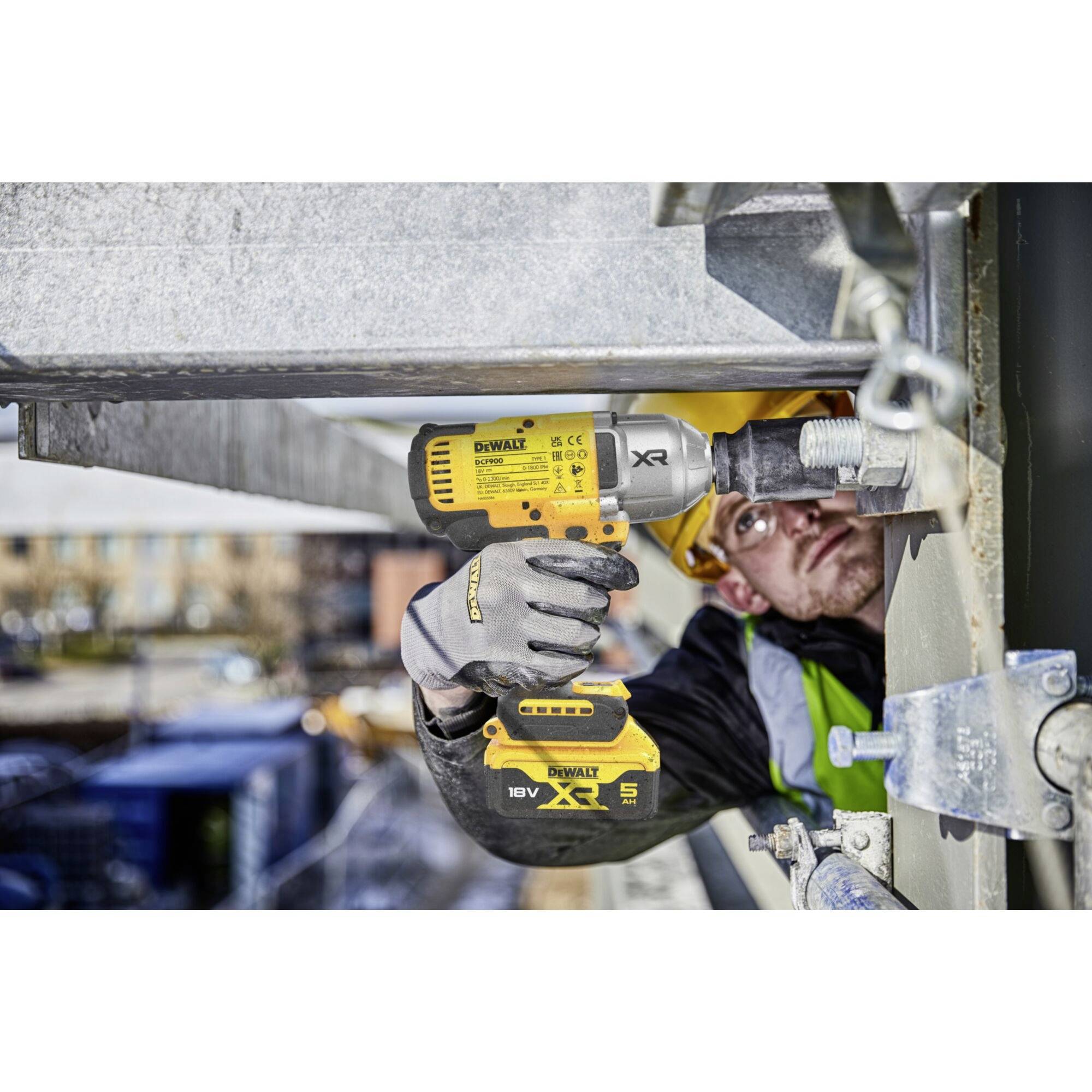 Ein Bauarbeiter zieht auf einer Baustelle mit einem Akkuschrauber eine Schraube fest. Er trägt Sicherheitskleidung und einen Helm.