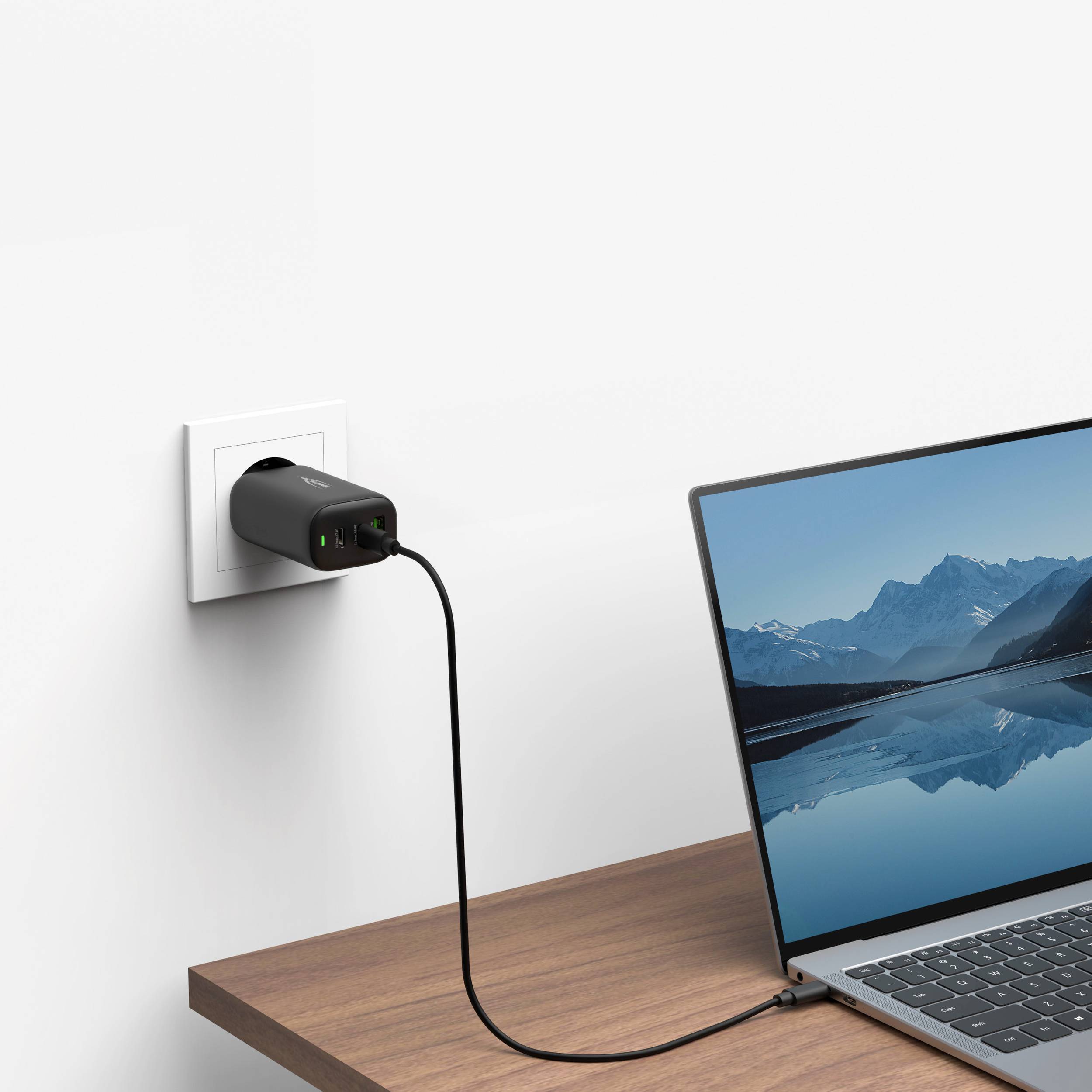 Ein Laptop ist an eine Steckdose angeschlossen und befindet sich auf einem Tisch. Der Stromadapter steckt in der Steckdose.