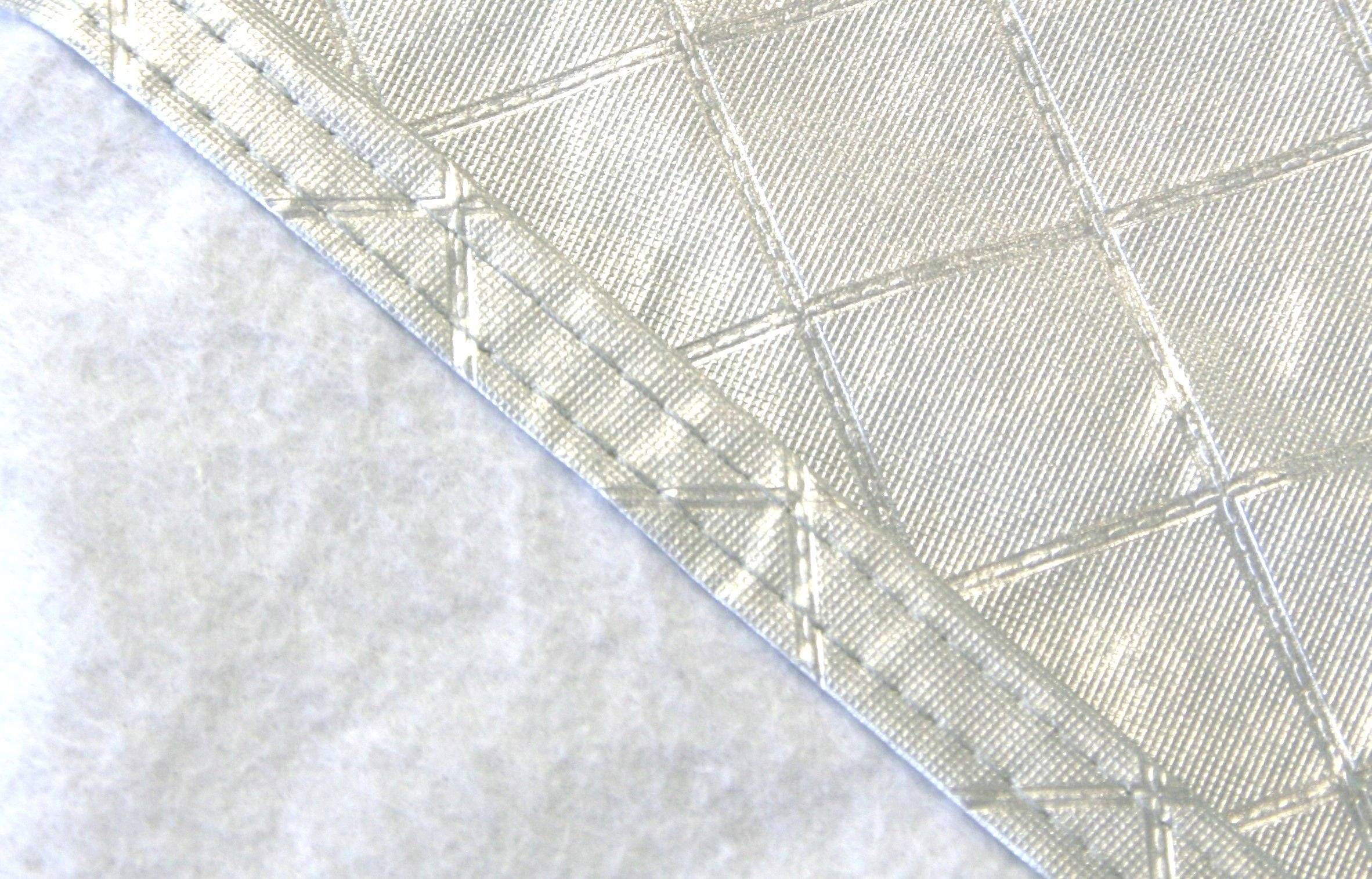 Nahaufnahme einer texturierten, gemusterten Stoffoberfläche in Beige mit diagonalen Nähten und einer einfarbigen, weißen Fläche darunter.