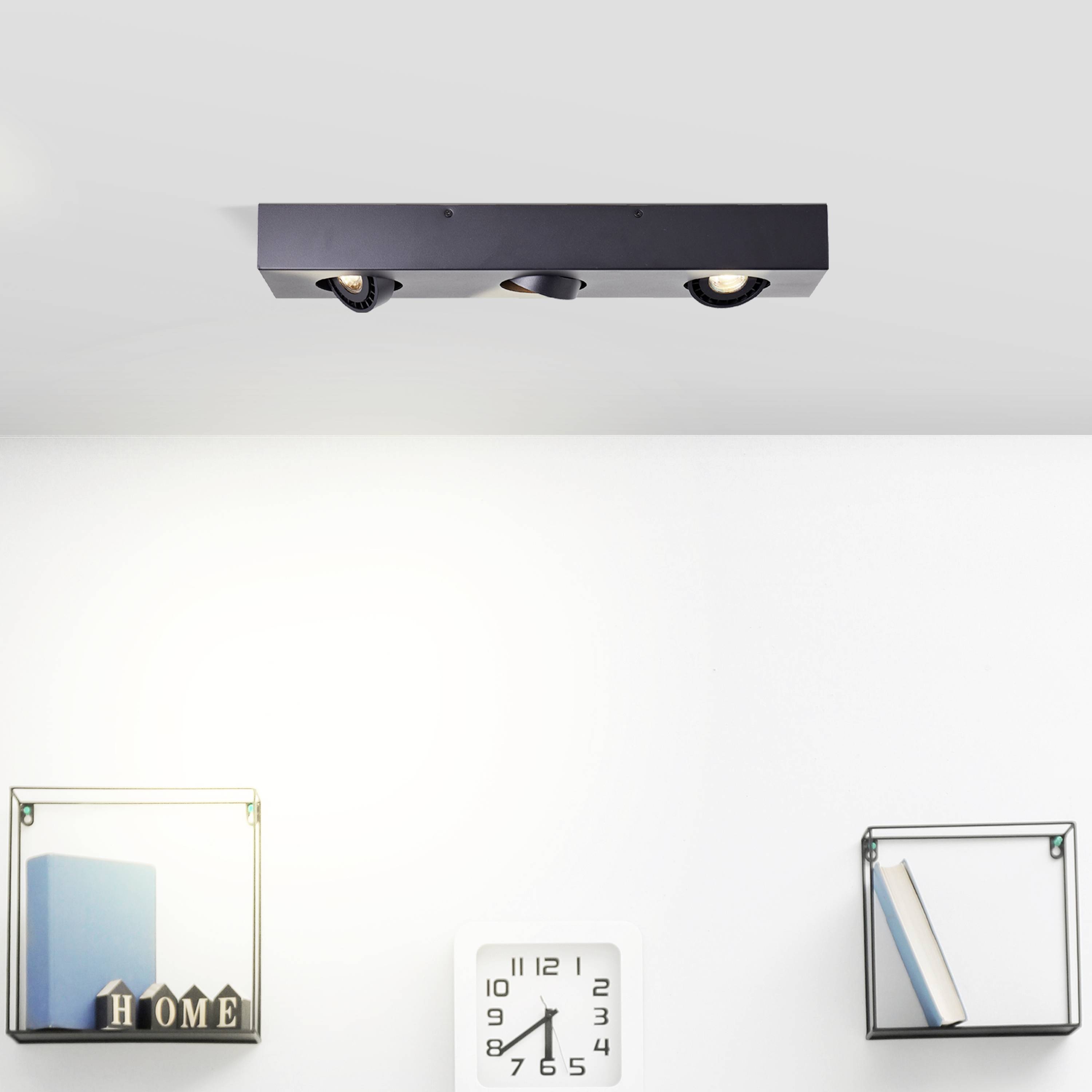 Deckenlicht mit zwei Spotleuchten, darunter zwei Regale mit Büchern und Dekoration. In der Mitte hängt eine Uhr an der Wand.