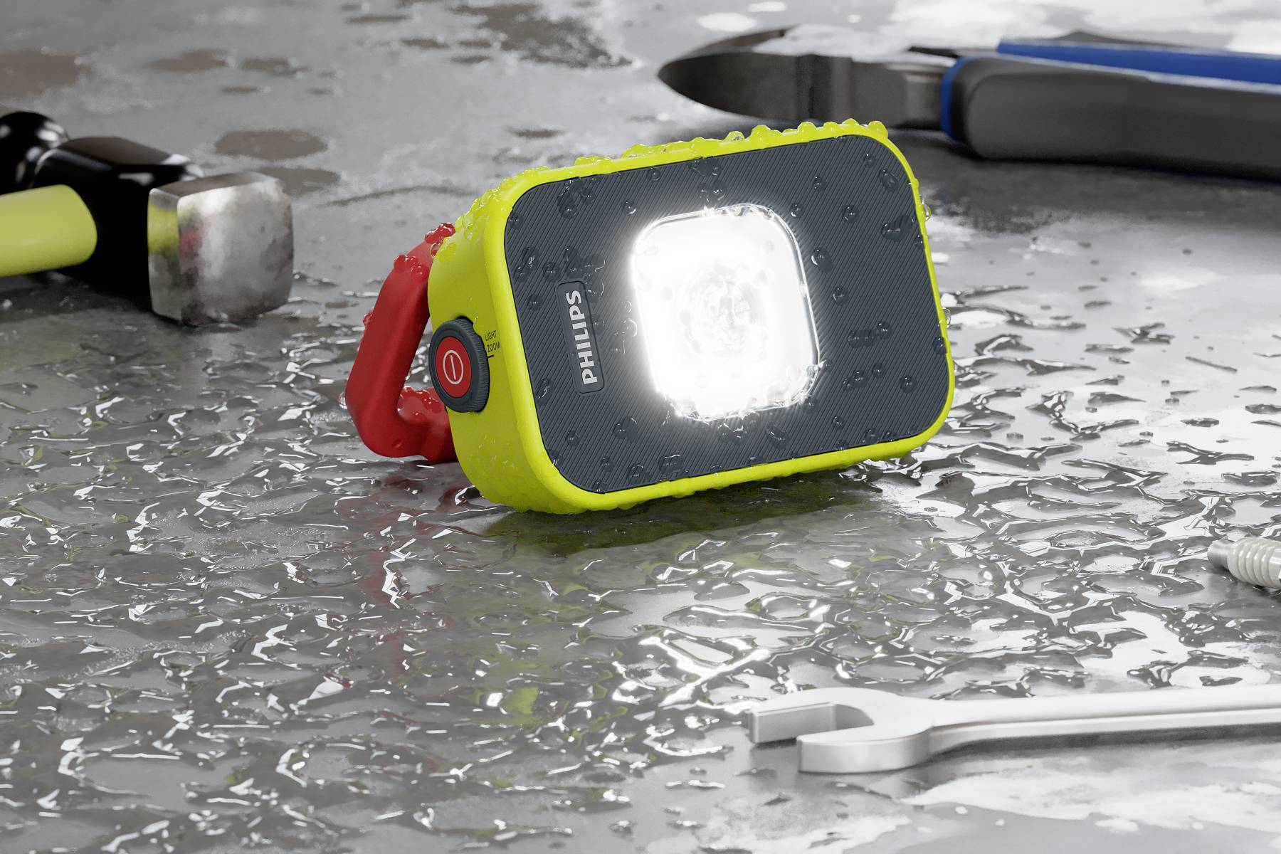 Eine leuchtende, spritzwassergeschützte Arbeitsleuchte liegt auf einem nassen Tisch neben einem Hammer, Schraubenschlüssel und einer Zange.