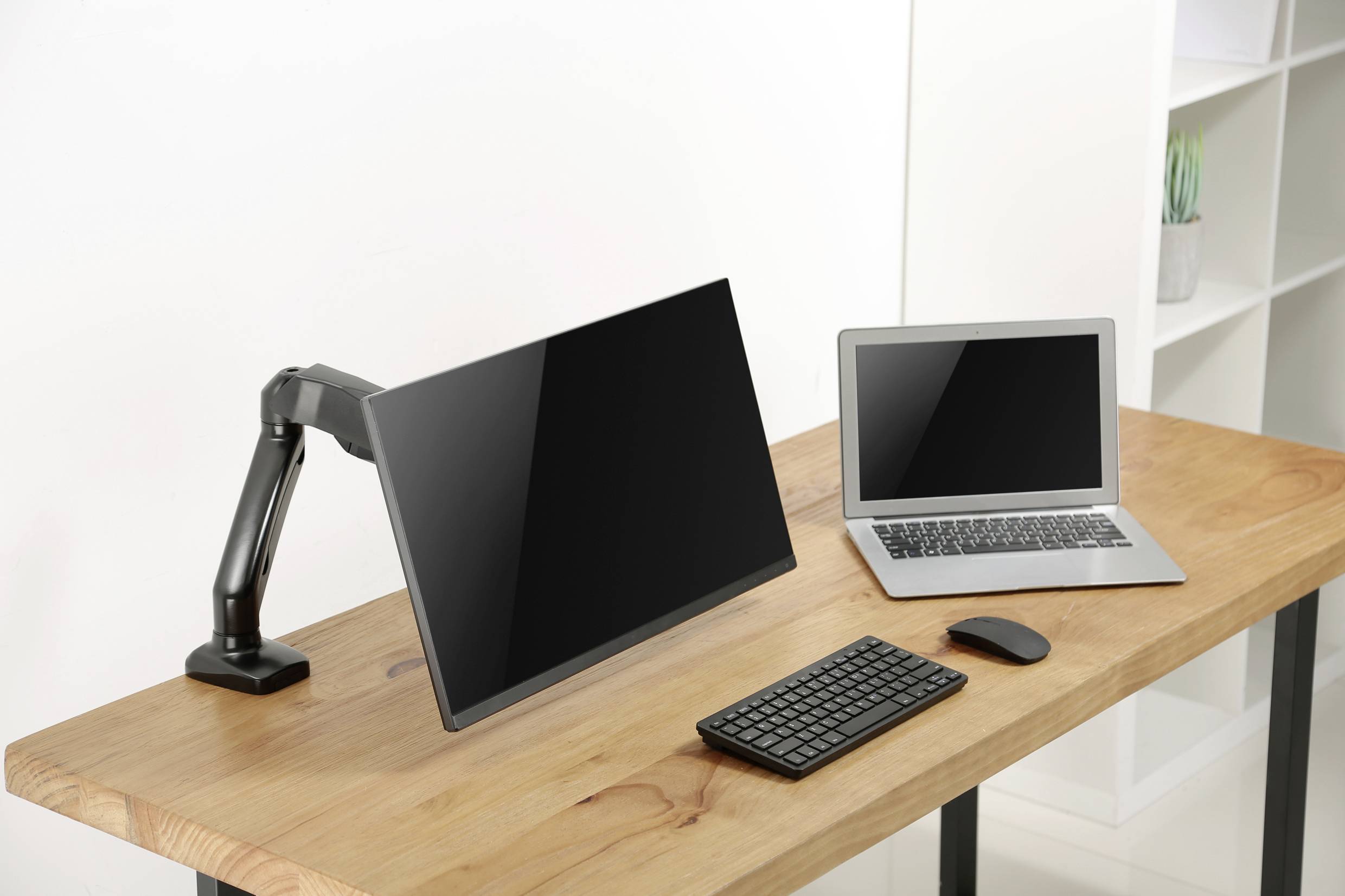 Ein Schreibtisch mit einem Laptop, einem großen, an einem Arm montierten Monitor, einer Tastatur und einer Maus.