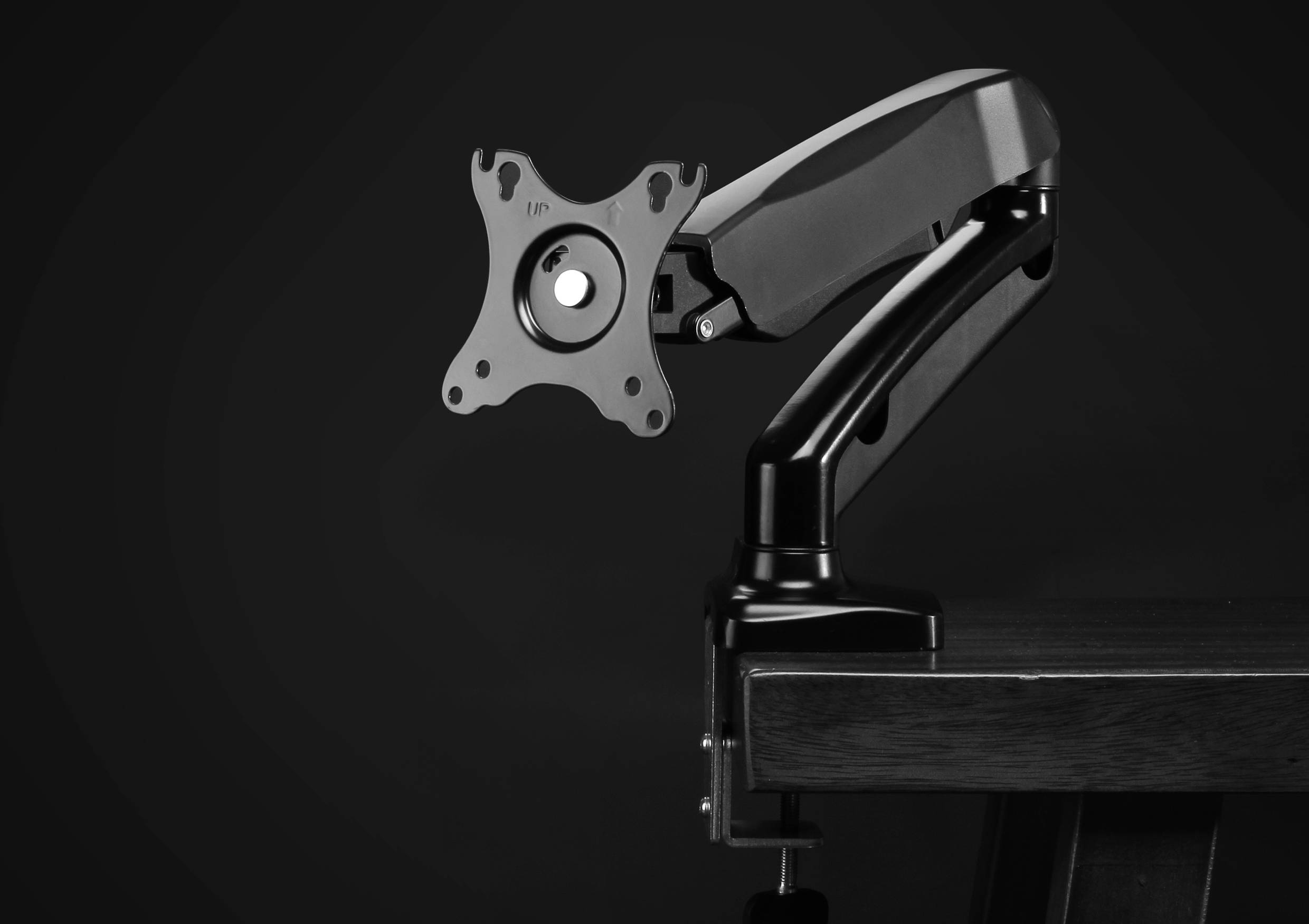 Ein schwarzer Monitorarm ohne Bildschirm ist an einen Schreibtisch montiert. Der Arm ist flexibel und verstellbar.