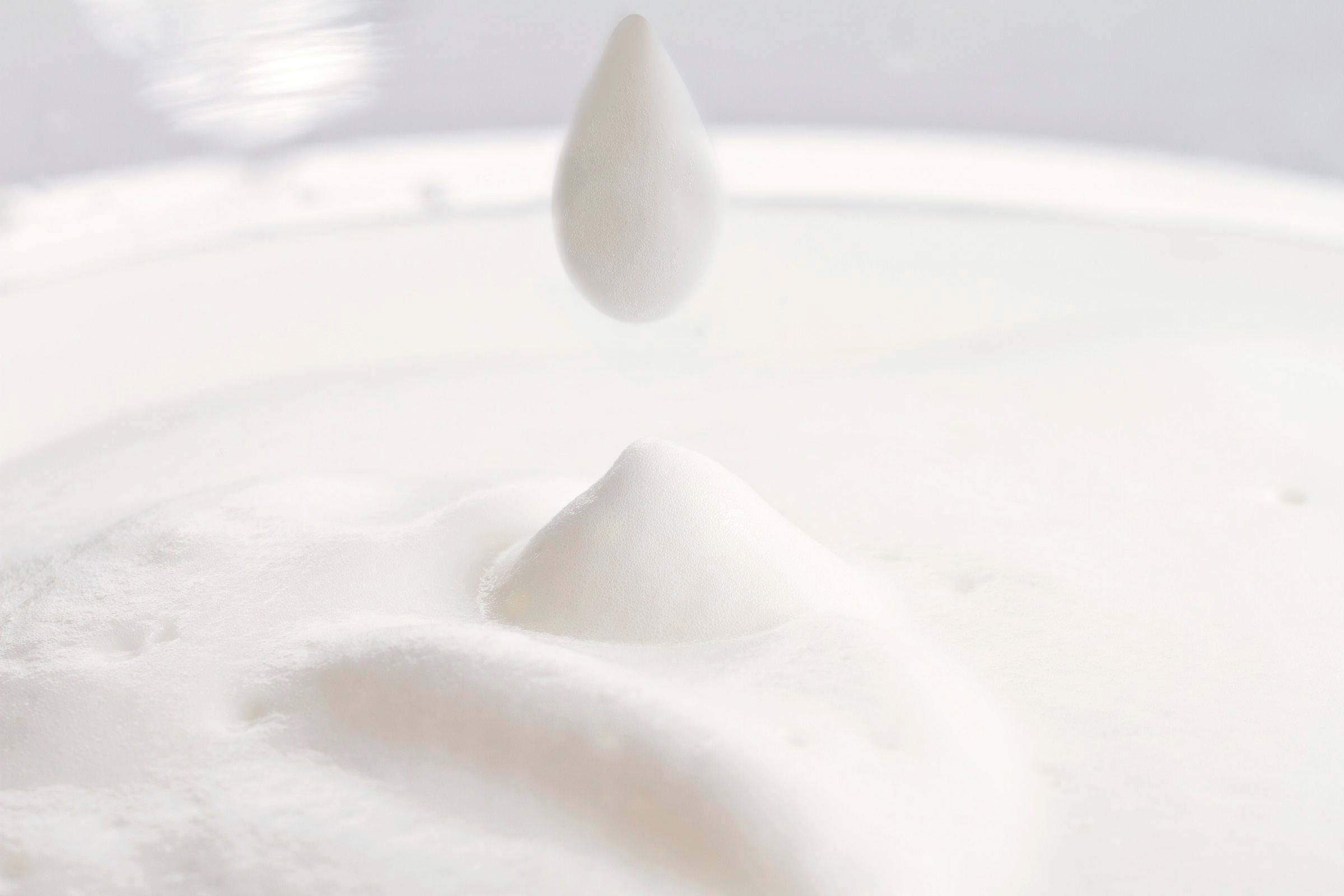 Ein Tropfen fällt in eine flüssige weiße Substanz, verursacht Wellen und eine kleine Spitze.