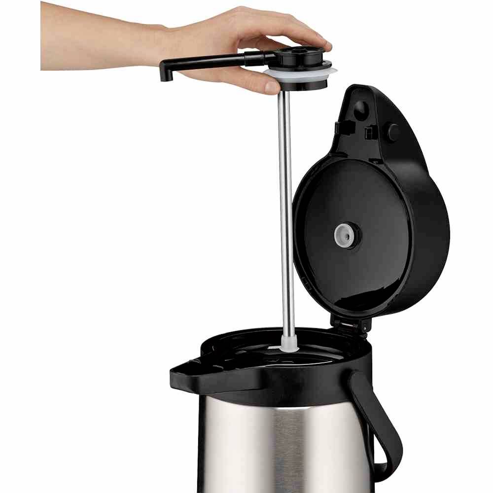 Eine Hand bedient die Pumpe einer silbernen Airpot-Kaffeekanne mit geöffnetem Deckel.