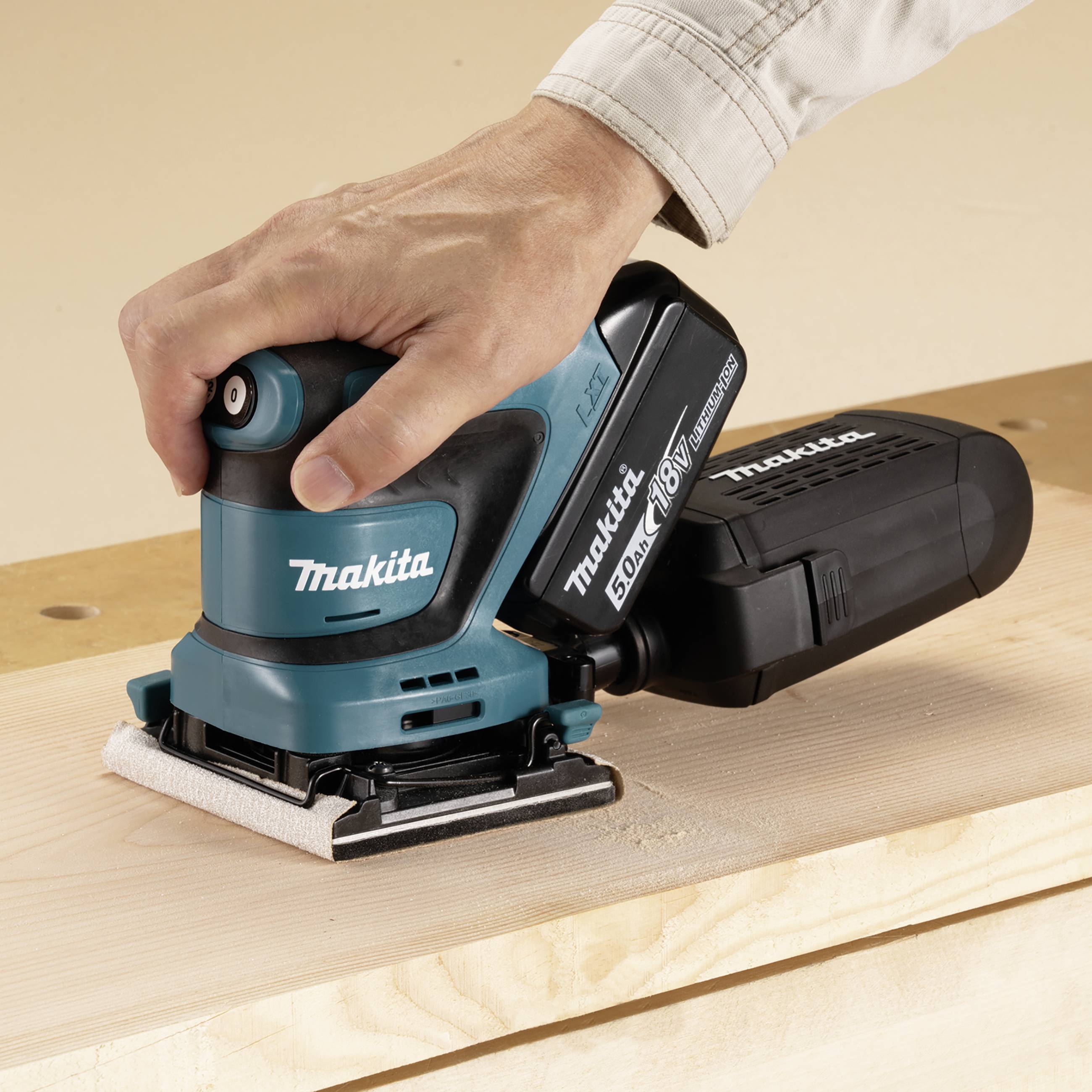 Ein Mensch schleift mit einem blauen elektrischen Schleifgerät eine Holzplatte. Der Schleifer trägt das Logo 'Makita' in weißer Schrift.