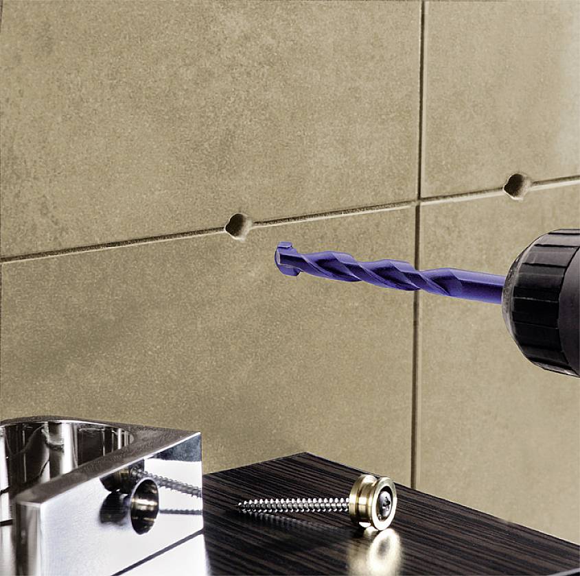 Eine Bohrmaschine bohrt ein Loch in eine geflieste Wand, während Schrauben und ein Schraubenzieher auf dem Tisch liegen.