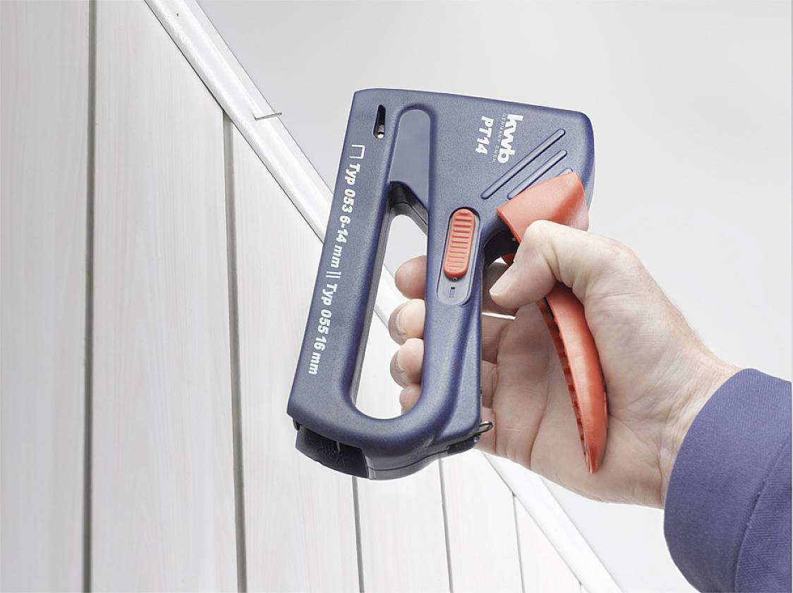 Eine Hand hält einen blauen Tacker, um eine Klammer in eine weiße Wand oder Oberfläche zu schießen.