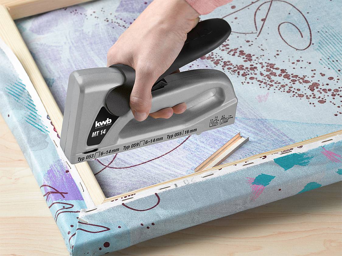 Jemand befestigt eine Leinwand auf einem Holzrahmen mit einem schwarzen und grauen Tacker.