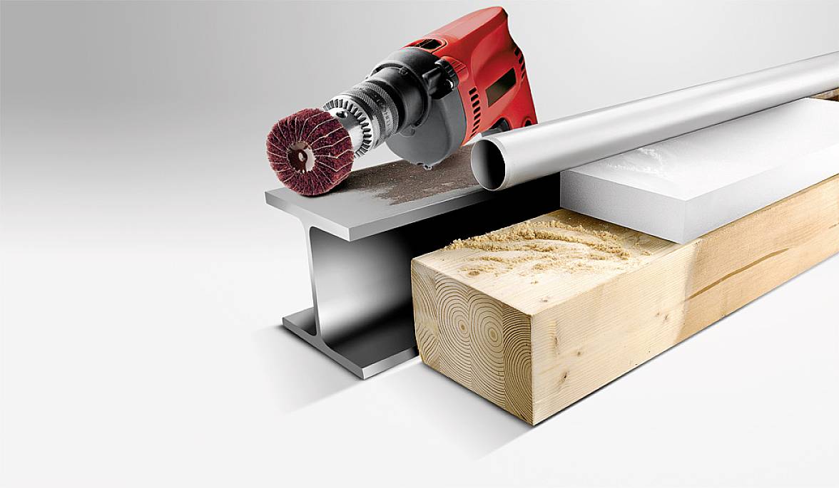 Eine rot-schwarze Bohrmaschine mit Schleifscheibe schleift Metall, Holz und PVC, die nebeneinander aufgereiht sind.
