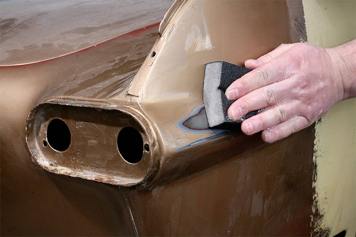 Eine Hand schleift die Oberfläche eines rostigen Autoteils mit einem Schleifschwamm, um es für die Lackierung vorzubereiten.
