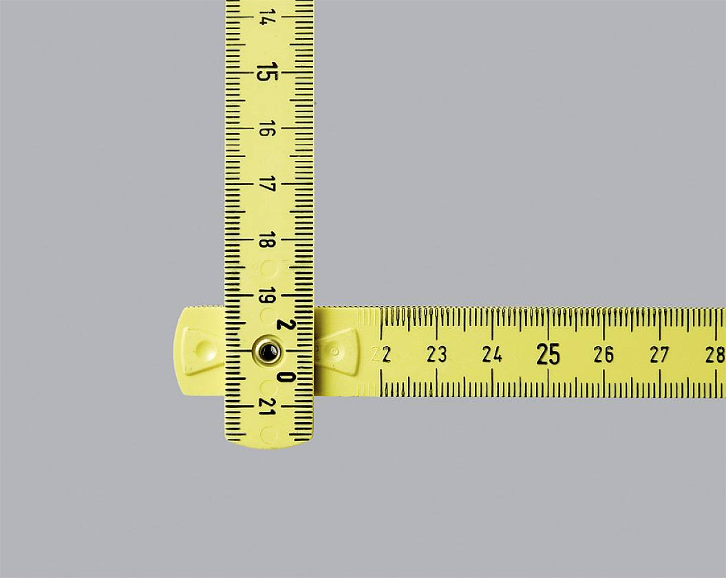 Gelber Zollstock in L-Form auf grauem Hintergrund. Der linke Abschnitt zeigt Zentimeter bis 16,5, der rechte Abschnitt zeigt bis 28,5 Zentimeter.