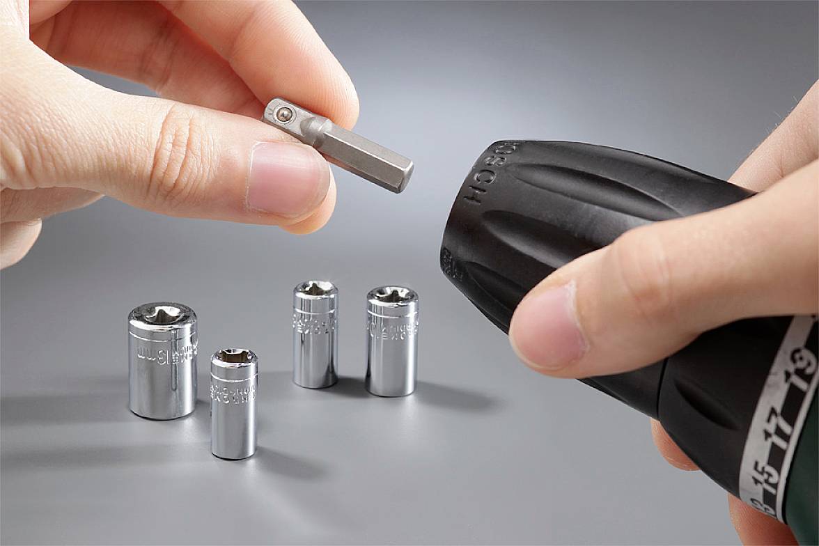 Hand hält Akkuschrauber und Bit; vier Steckschlüssel liegen daneben. Werkzeugwechsel wird gezeigt.