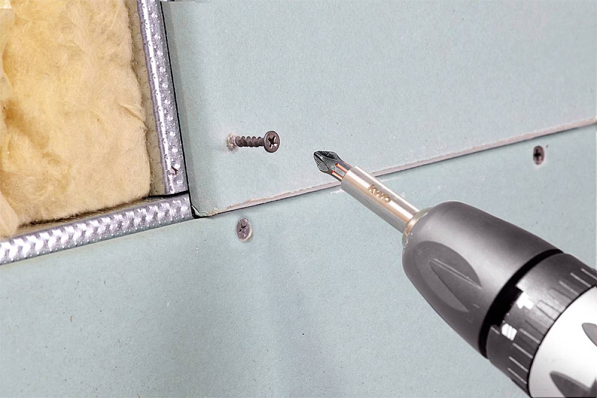Ein Akkubohrer zieht eine Schraube in eine Gipsplatte, die an einem Metallrahmen befestigt ist. Dahinter ist Isoliermaterial sichtbar.