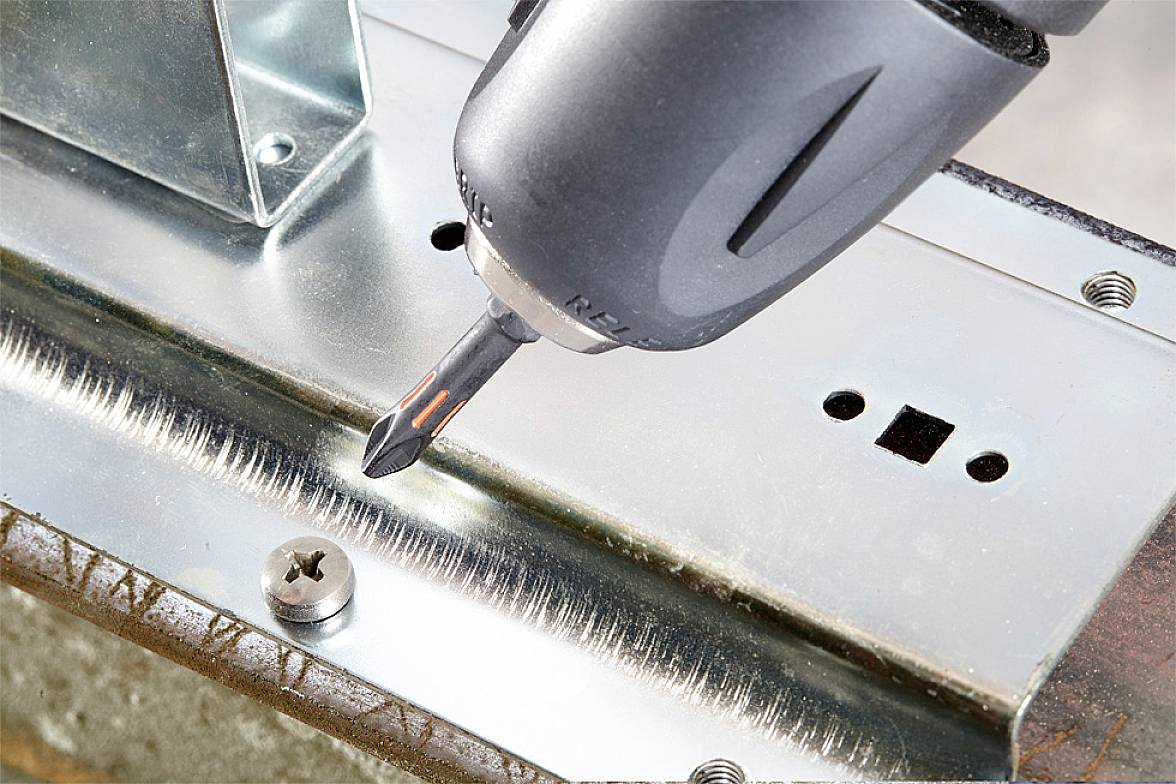 Akkubohrer zieht Schraube in ein Metallblech an, das auf einem strukturierten Untergrund liegt.