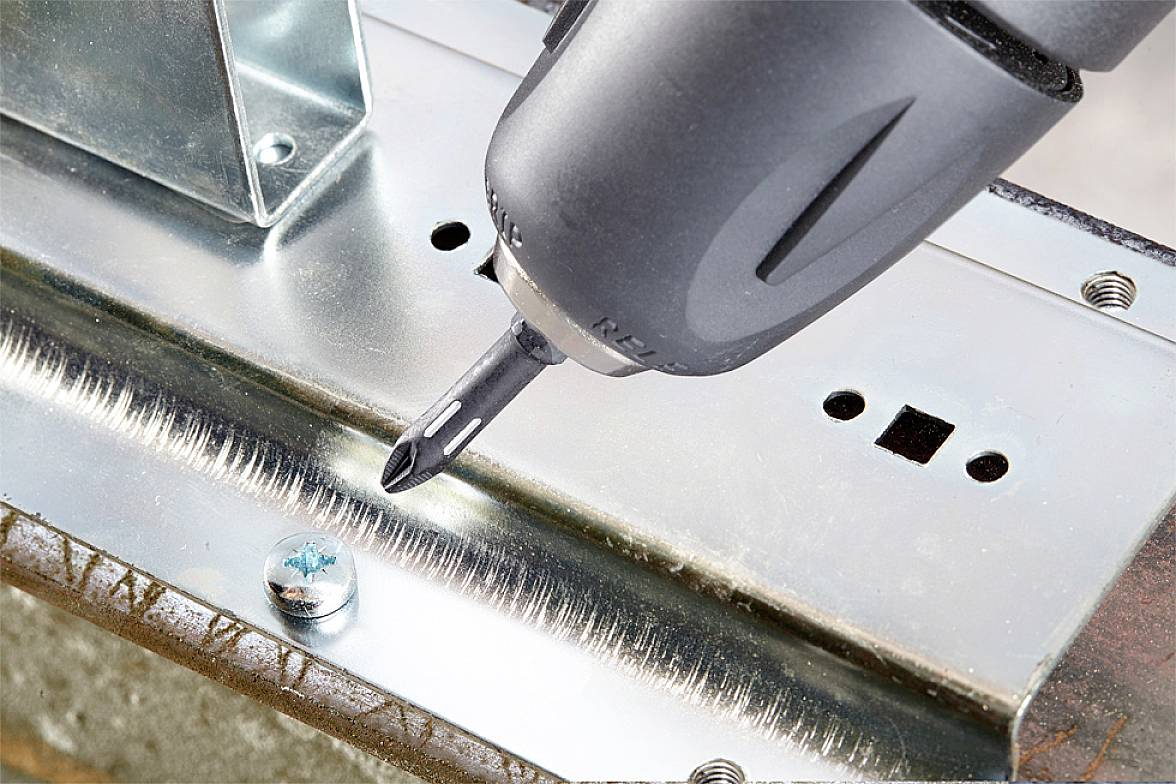 Akkubohrer zieht Schraube in eine Metallplatte ein, zeigt Handwerkerarbeit an Metallkonstruktion.