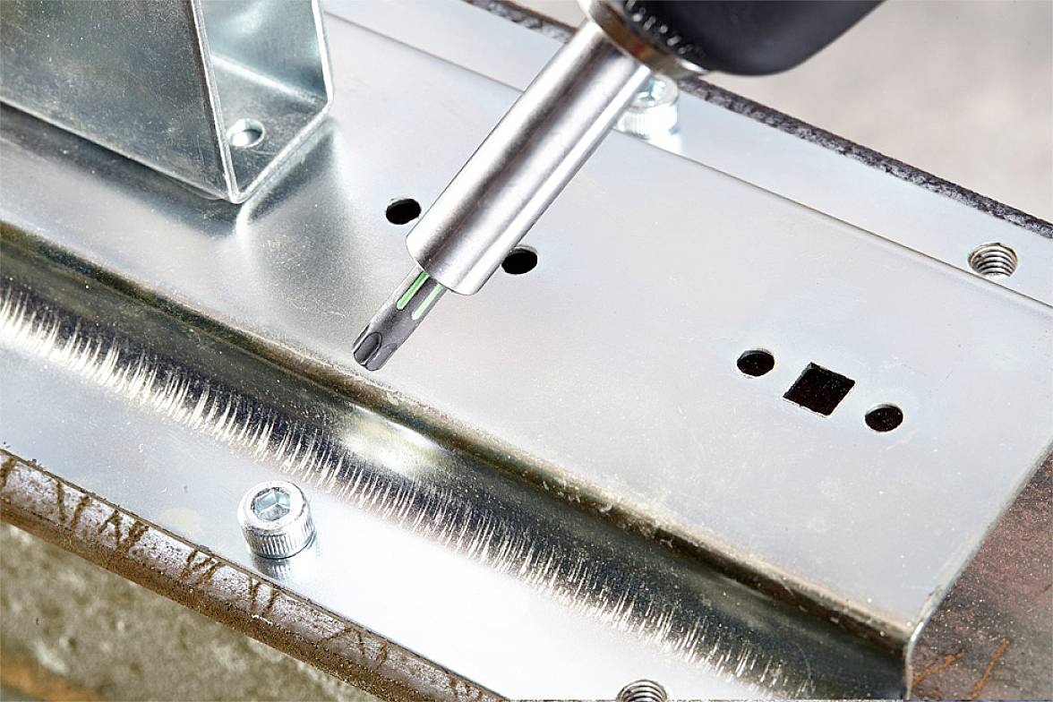 Nahaufnahme eines elektrischen Schraubendrehers, der eine Schraube in ein Metallteil dreht. Hauptfokus liegt auf dem Werkzeug und dem Schraubvorgang.