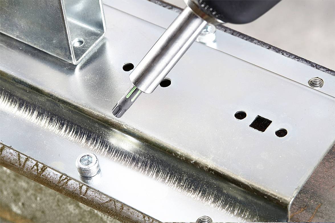 Schraubendreher zieht eine Schraube in eine Metallfläche ein. Nahaufnahme zeigt präzise Verschraubung und stabilisierende Metallteile.