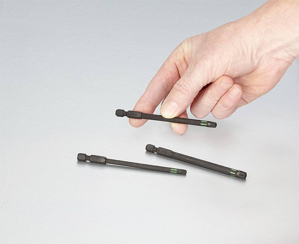 Eine Hand hält einen schwarzen Bohrer mit grünem Ring, zwei weitere liegen daneben auf der grauen Oberfläche.