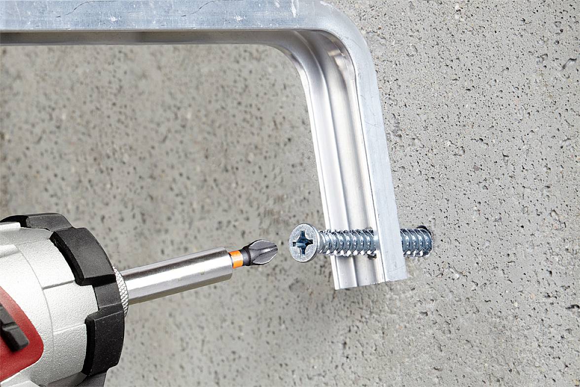 Ein Bohrer zieht eine Schraube in eine Metallhalterung an einer Betonwand fest.
