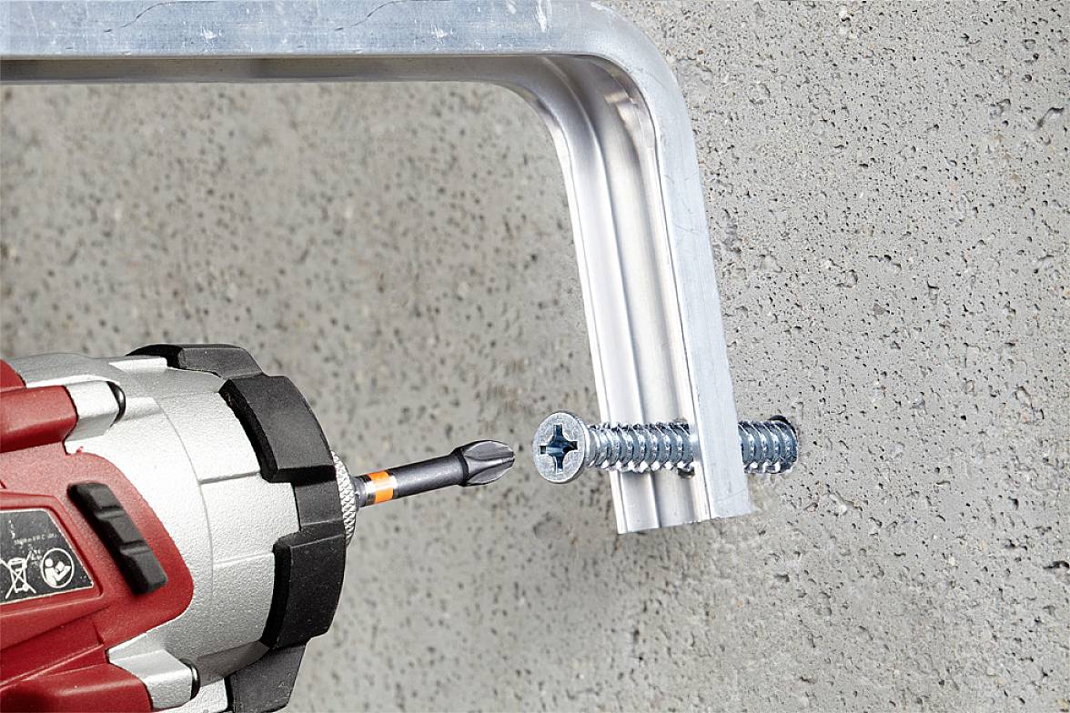 Akkuschrauber zieht Schraube in Metallwinkel, der an Betonwand befestigt wird.