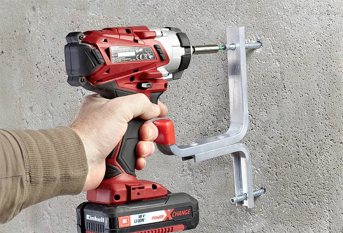 Ein Akkuschrauber in einer Hand befestigt ein Metallteil mit Schrauben an einer Betonwand.