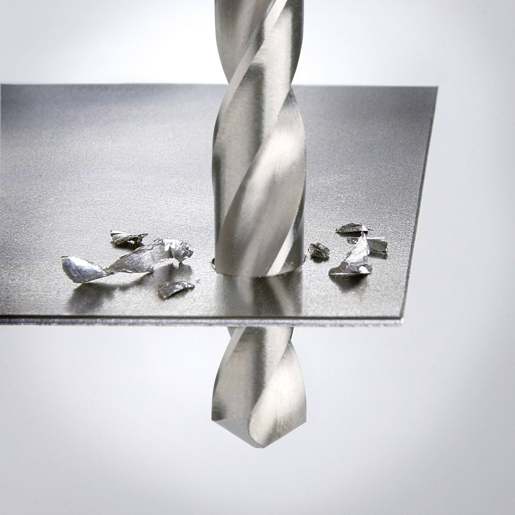 Ein Bohrer durchbohrt ein Blech von oben. Metallspäne liegen um das Loch.