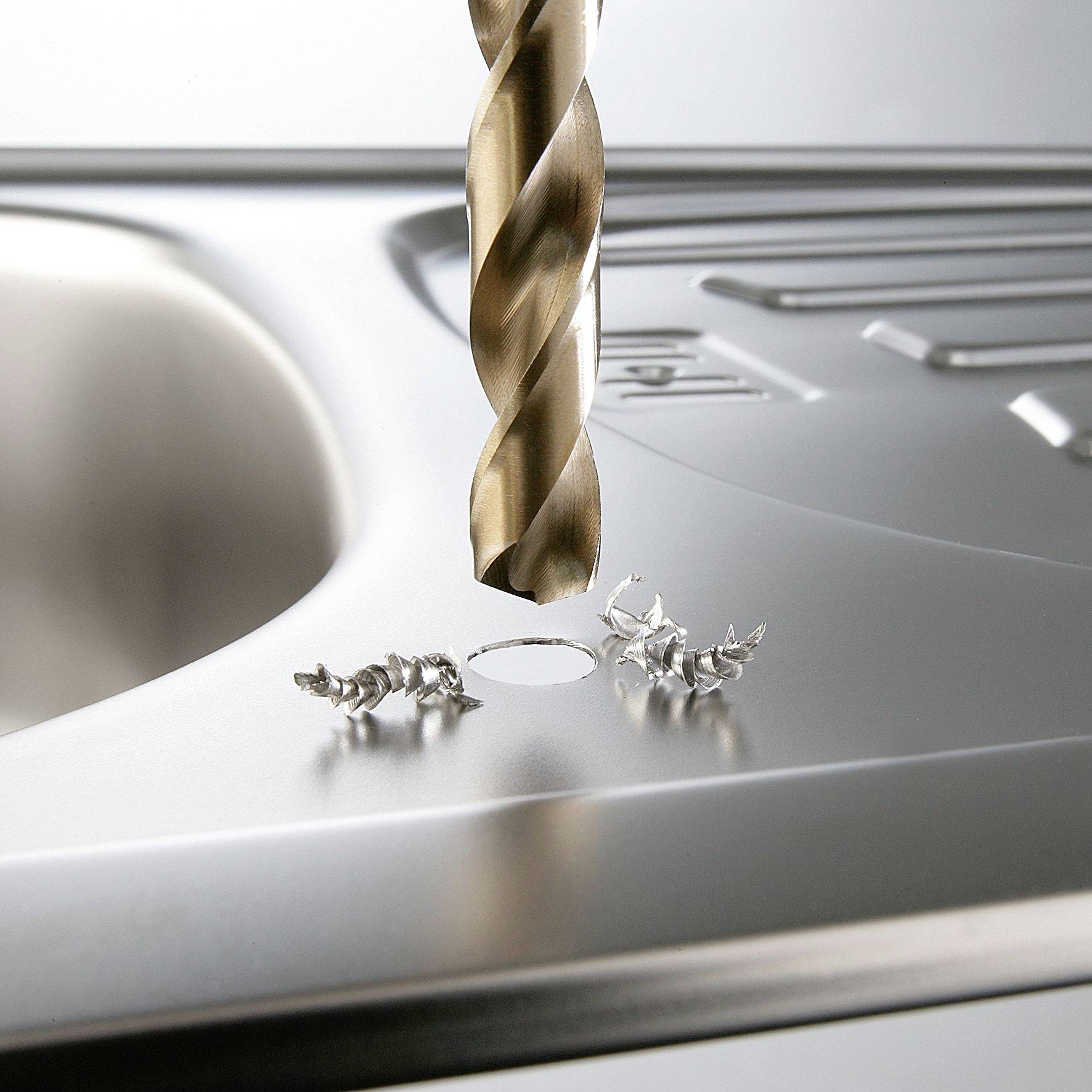 Nahaufnahme eines Bohrers, der ein Loch in eine Edelstahloberfläche bohrt. Metallspäne um das gebohrte Loch herum.