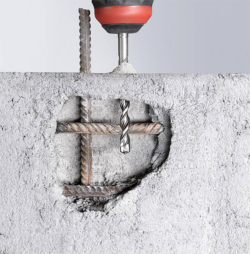 Ein Bohrer durchdringt eine Betonwand mit Stahlarmierung. Der Bohrer zeigt, wie Bewehrungsstäbe durch den Beton verlaufen.