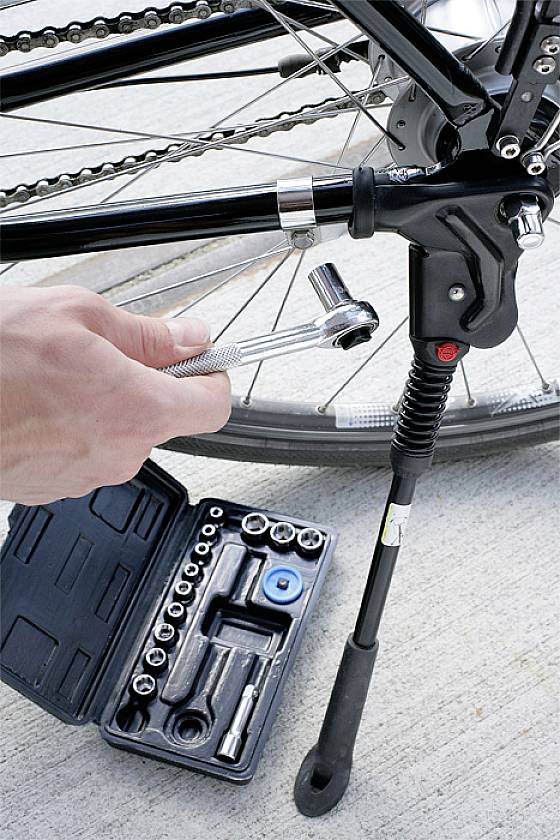 Person schraubt mit Ratsche an Fahrradständer, daneben Werkzeugset auf Beton.