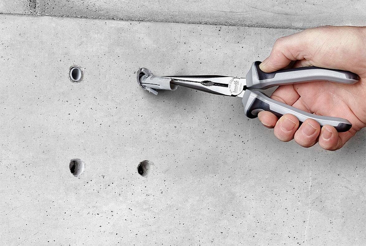 Eine Hand hält eine Zange, die einen Dübel aus einer Betonwand zieht.