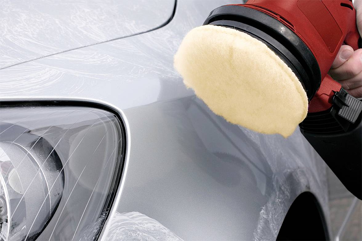 Eine Poliermaschine wird verwendet, um den Lack eines silbernen Autos zu polieren, wobei das vordere Fahrzeuglicht zu sehen ist.