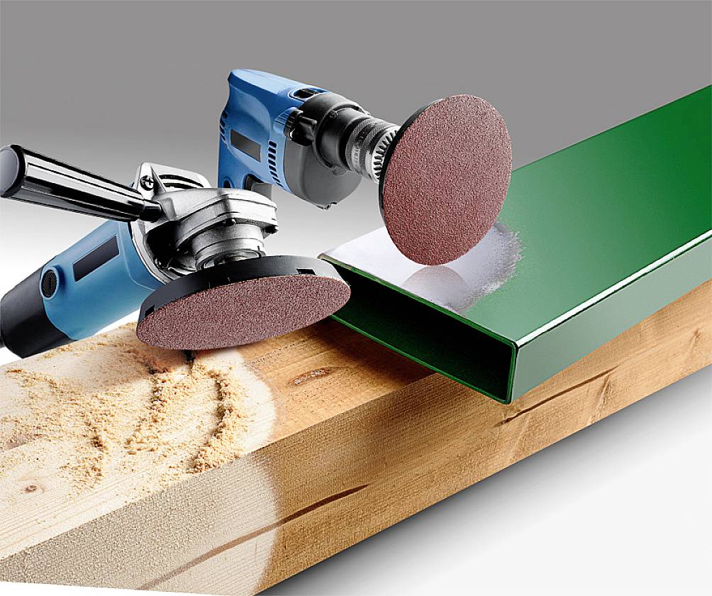 Zwei Schleifmaschinen bearbeiten Holz und Metall: Eine Maschine schleift Holz mit Sägemehl, die andere poliert ein grün lackiertes Metallstück.