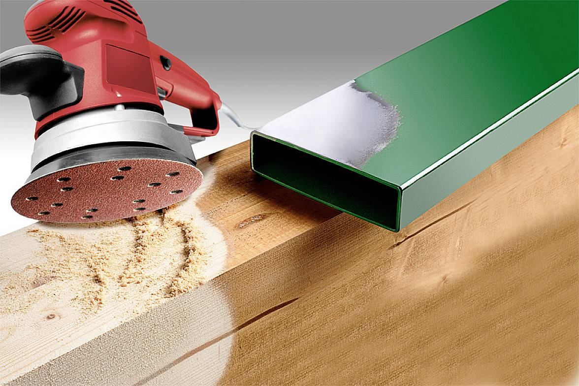 Eine rote Schleifmaschine schleift ein Holzbrett, während nebenan ein grüner Metallbalken liegt.