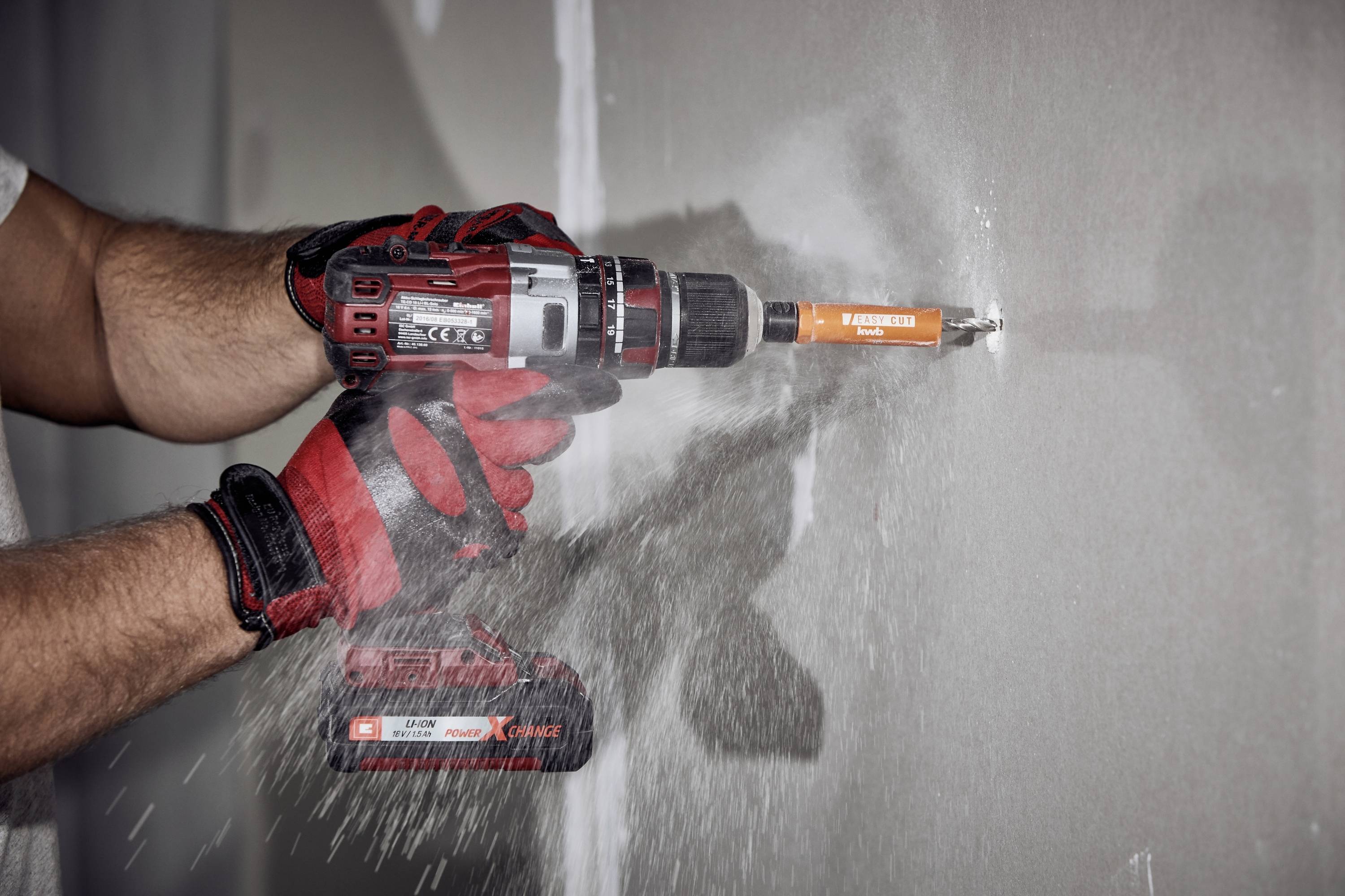 Eine Person bohrt mit einem Akku-Bohrschrauber ein Loch in eine Wand, während Staub aufgewirbelt wird.
