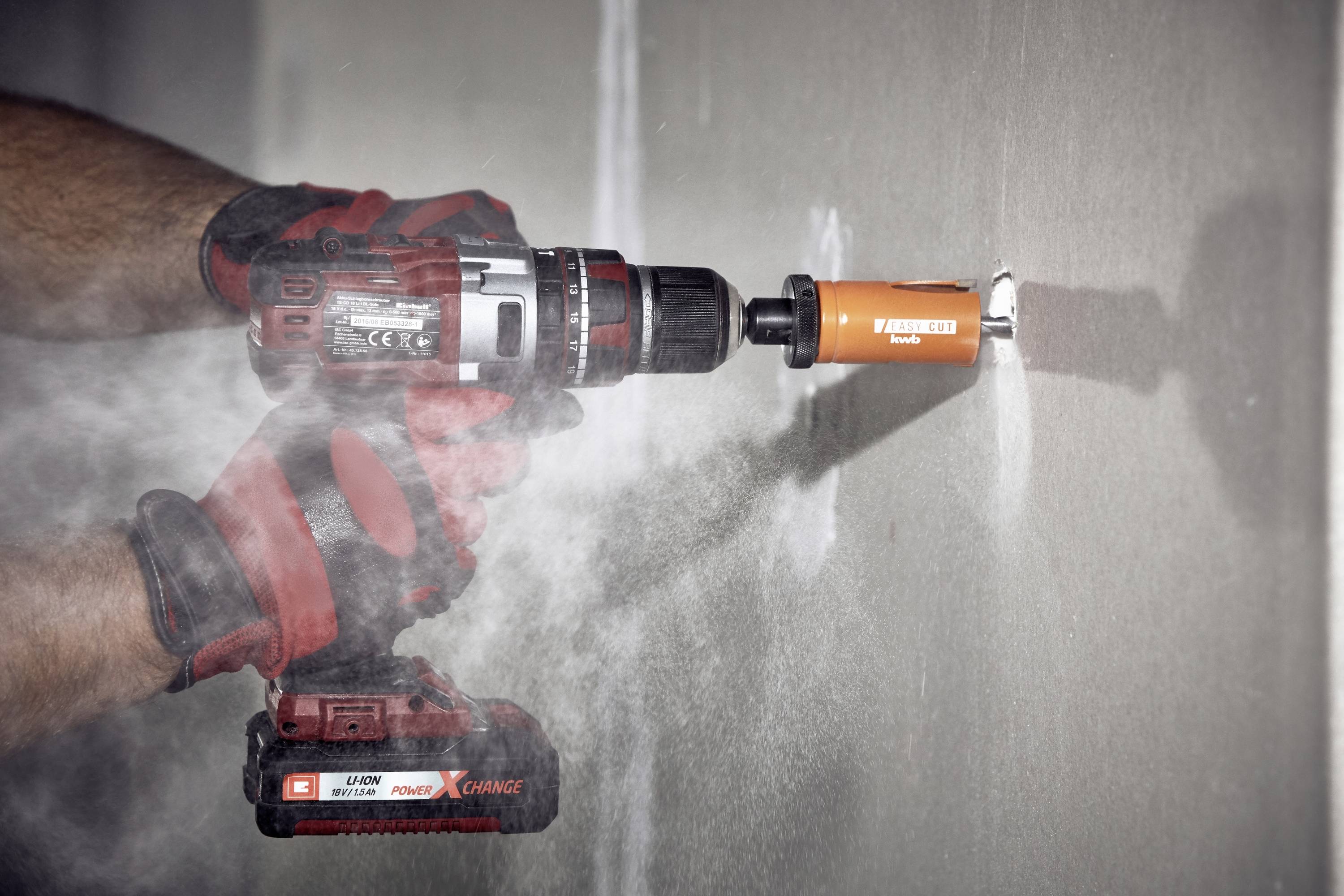 Eine Person bohrt mit einem Akkuschrauber ein Loch in eine Wand. Staub entsteht durch die Bohrung.