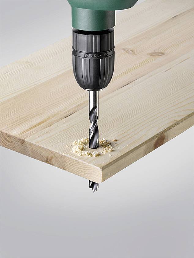 Eine Bohrmaschine bohrt ein Loch in ein Brett. Holzwirbel sind um den Bohrer herum sichtbar.