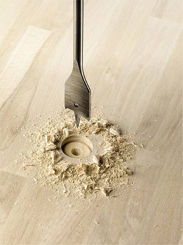 Bohrer bohrt ein rundes Loch in eine helle Holzoberfläche, umgeben von Holzspänen.