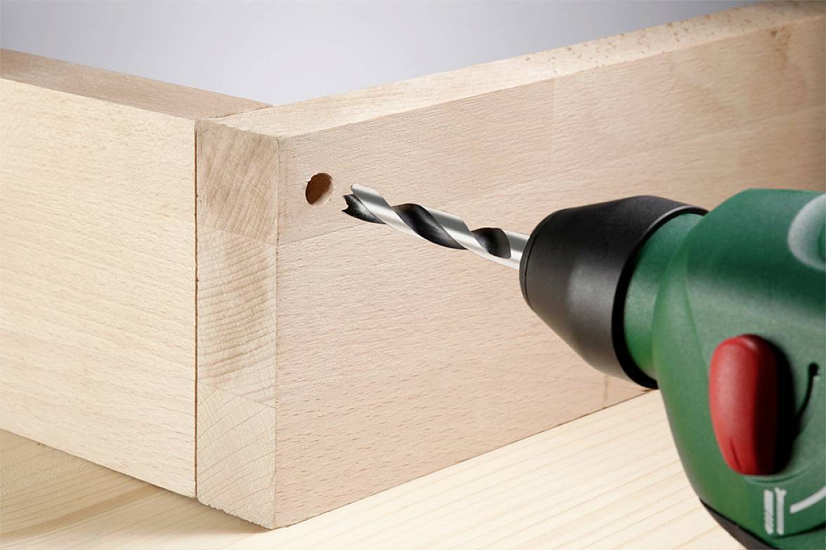 Bohrer beim Bohren eines Lochs in einem Holzbrett. Nahaufnahme zeigt, wie der Bohrer das Holz durchdringt.