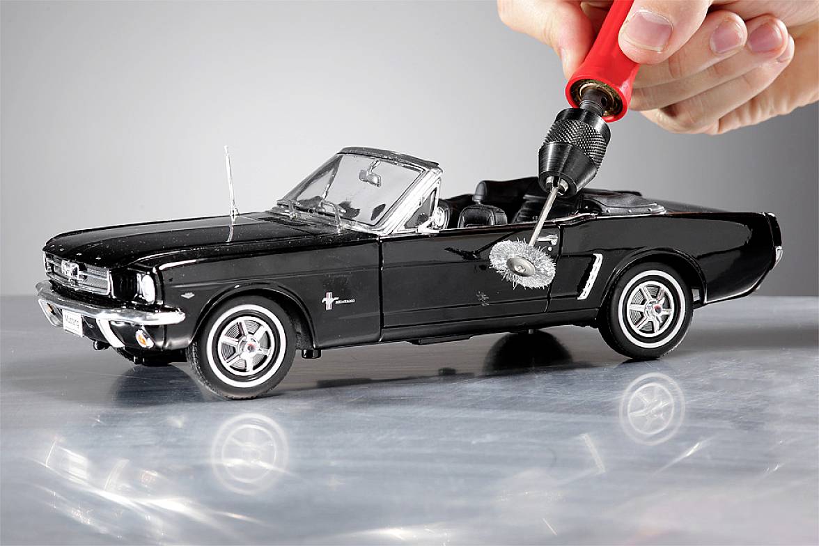 Ein Modellauto eines schwarzen Ford Mustang Cabriolets wird mit einer roten Bohrmaschine bearbeitet, die einen kleinen Schleifaufsatz hat.