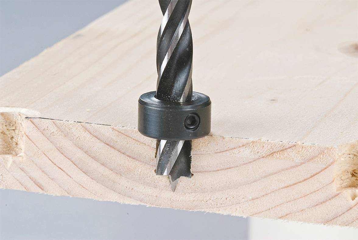Ein schwarzer Bohrer durchbohrt ein Holzstück. Ein Stoppring ist am Bohrer befestigt, um die Tiefe des Bohrlochs zu kontrollieren.