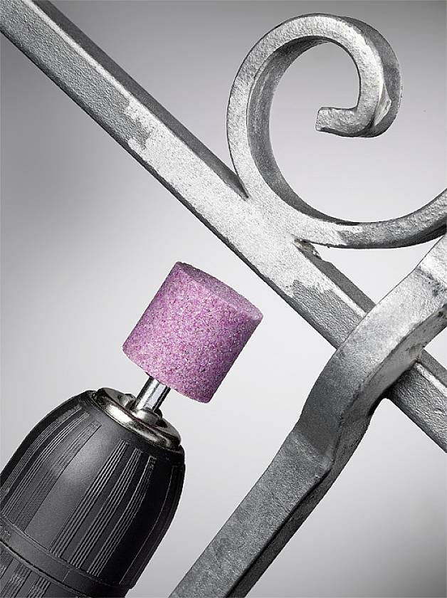 Ein Bohrer mit einem rosa Schleifaufsatz poliert die Oberfläche eines geschwungenen Metallgeländers.