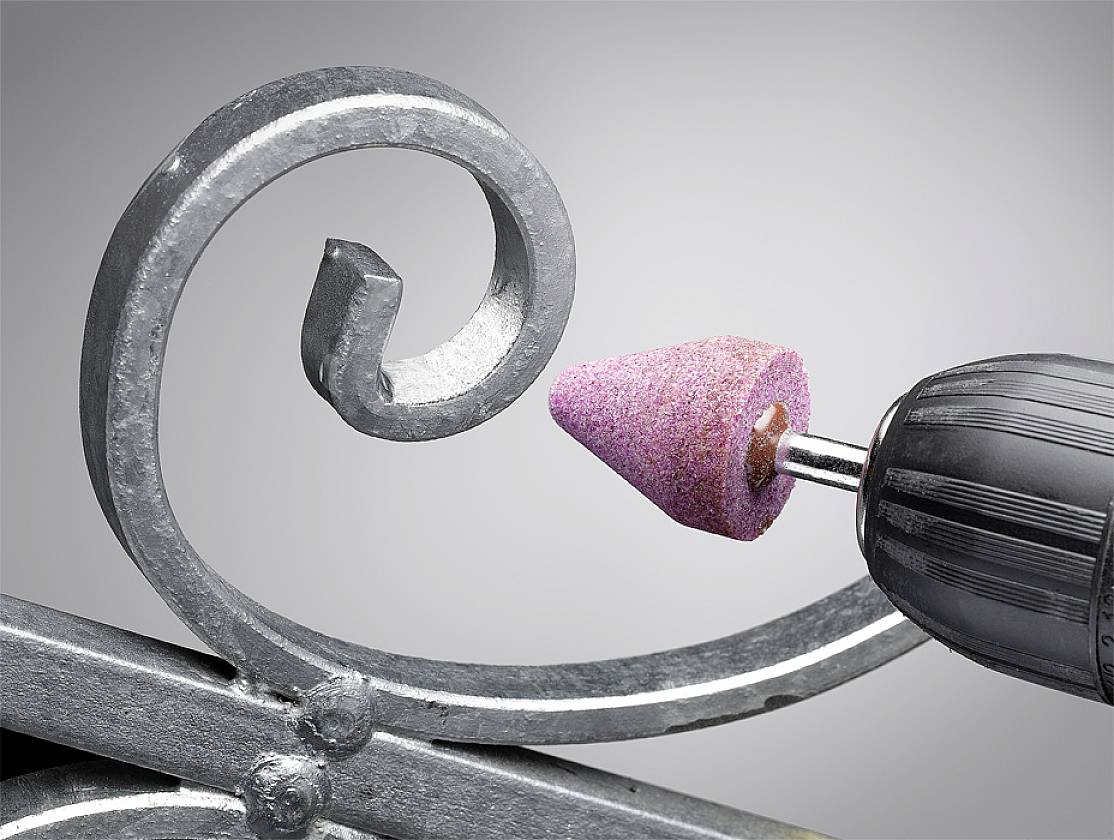 Ein metallischer Bohrer mit rosa Schleifaufsatz bearbeitet dekoratives Metallstück, zeigt präzise Handwerksarbeit und Detailbearbeitung.