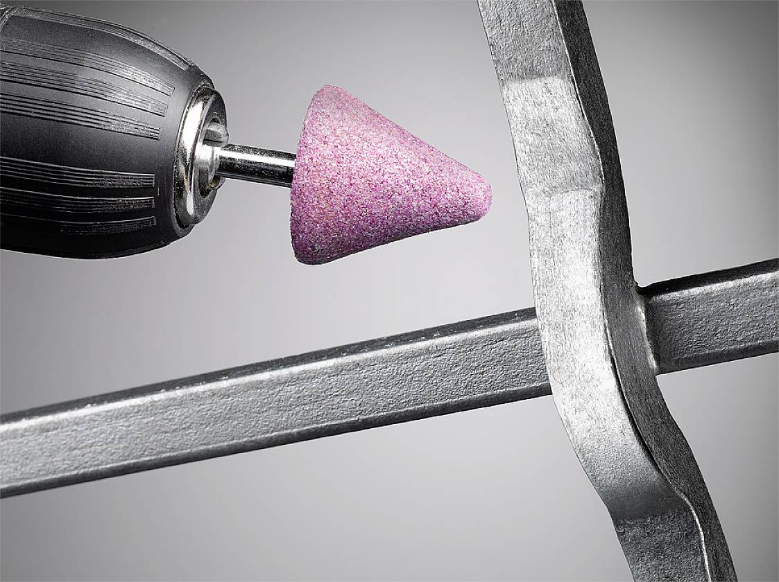Nahaufnahme eines Drehwerkzeugs mit pinkem Schleifkopf, das an einer Metallkante arbeitet.