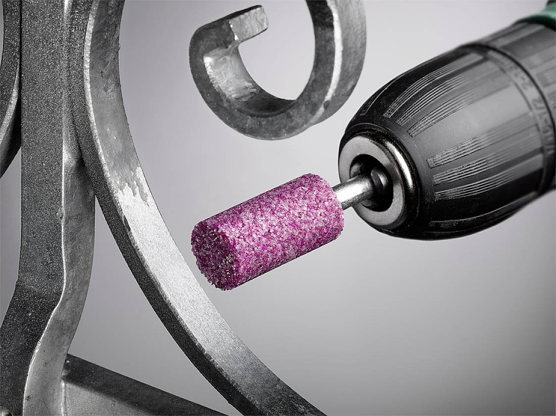 Eine elektrische Bohrmaschine mit einem rosa Schleifkopf bearbeitet ein Metallwerkstück mit geschwungenen Details.