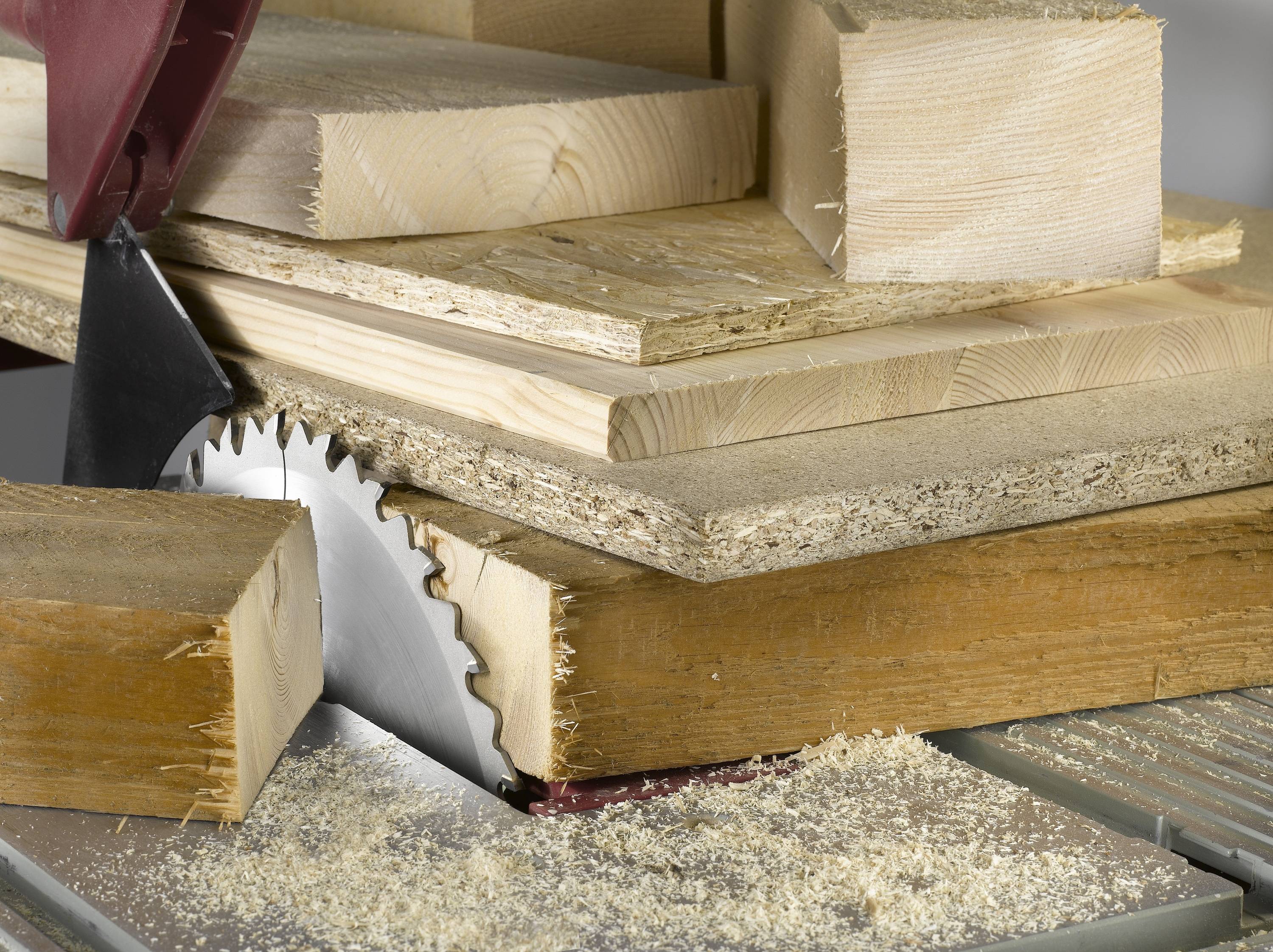Holzbearbeitung: Stapel aus verschiedenen Holzplatten und Balken auf einer Kreissäge, Späne sichtbar.
